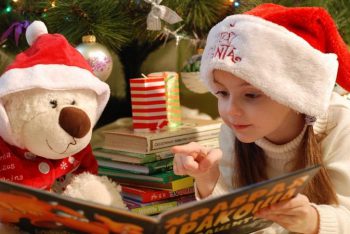 Ein Mädchen liest ihrem Teddy aus einem Weihnachtsbuch für Kinder vor