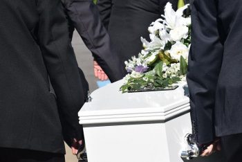 Sarg mit Blumenschmuck wird von Trägern zur Grabstätte getragen.