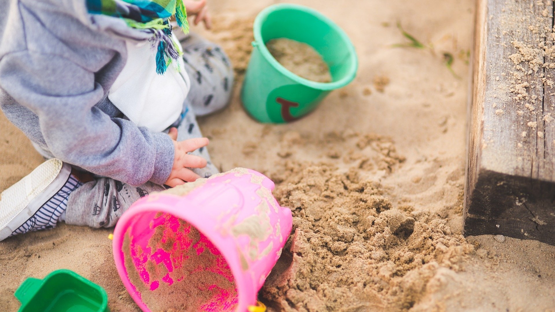 Ein Kind sitzt im Sandkasten und spielt.